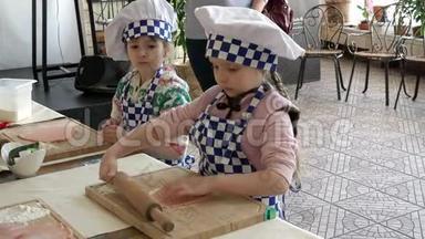 两个穿制服的小女孩，厨师学着用<strong>擀面杖在木板上</strong>擀面